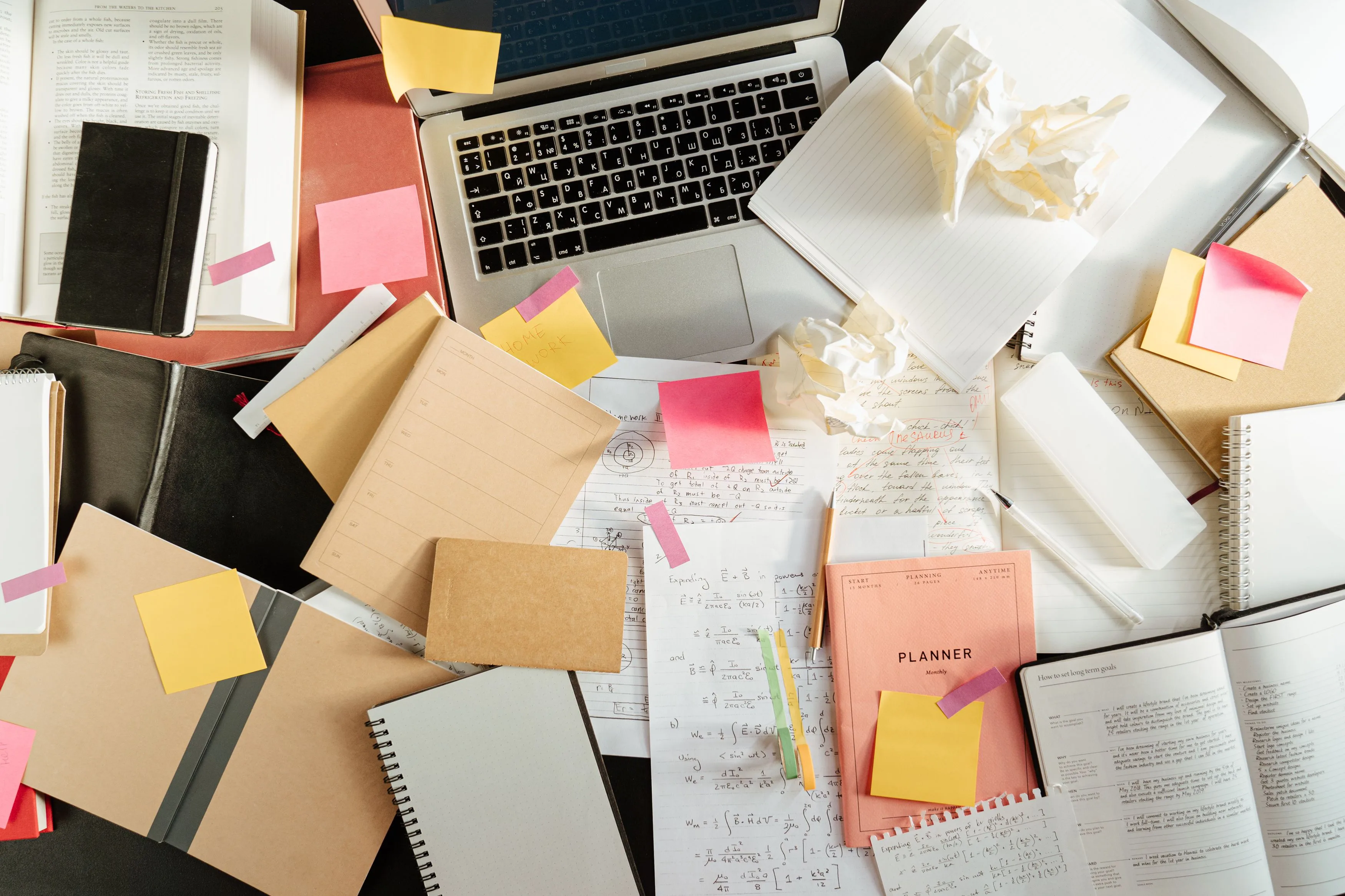 Desk with laptop, notebooks, and sticky notes for keyword brainstorming
